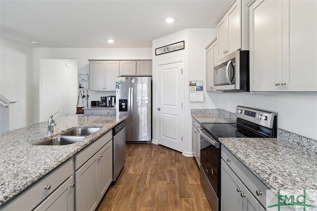 kitchen with sink, gray cabinetry, dark hardwood / wood-style flooring, stainless steel appliances, and light stone countertops