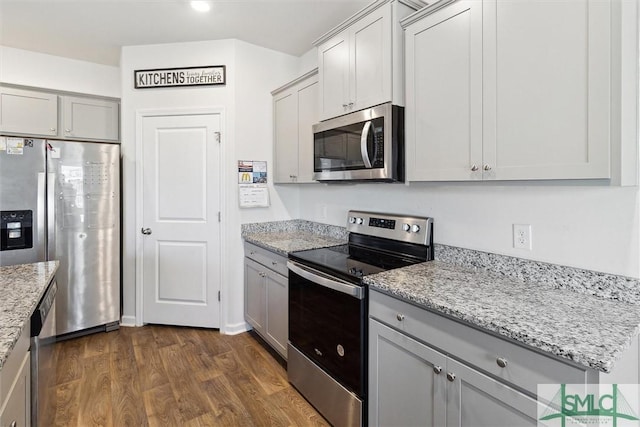 kitchen with dark wood-type flooring, appliances with stainless steel finishes, gray cabinets, and light stone counters