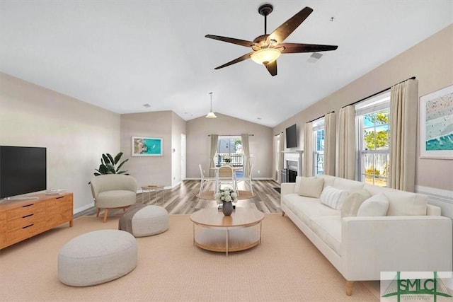 living room with baseboards, ceiling fan, vaulted ceiling, a fireplace, and wood finished floors