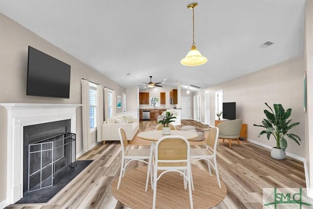 dining space with light wood-type flooring, visible vents, a fireplace, and vaulted ceiling