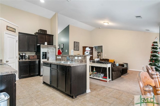 kitchen with vaulted ceiling, appliances with stainless steel finishes, an island with sink, sink, and light colored carpet