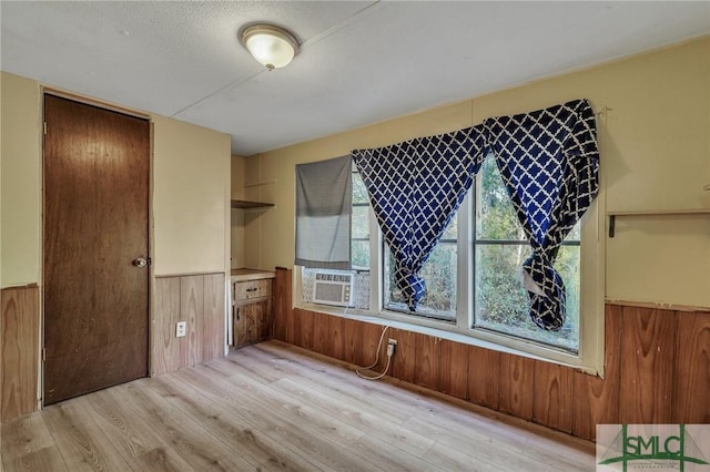 interior space featuring cooling unit, a textured ceiling, wooden walls, and light hardwood / wood-style flooring