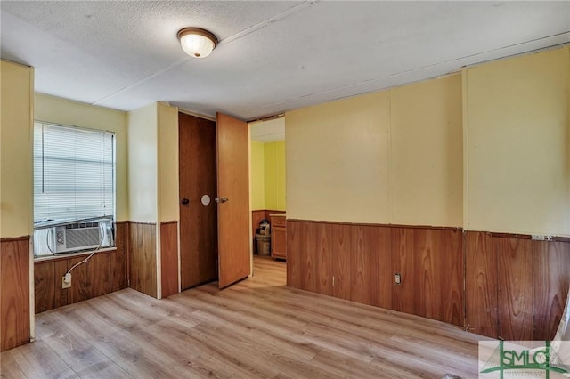 empty room with cooling unit, a textured ceiling, and light hardwood / wood-style flooring