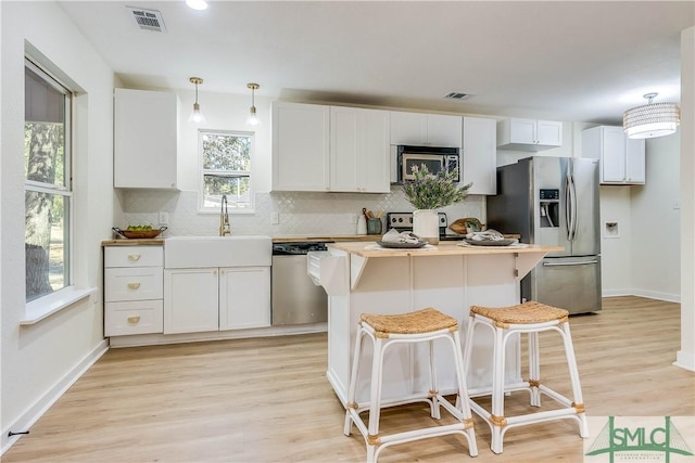 kitchen with hanging light fixtures, light wood-type flooring, white cabinets, and appliances with stainless steel finishes