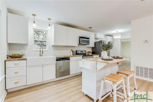 kitchen with pendant lighting, sink, a breakfast bar, appliances with stainless steel finishes, and white cabinetry