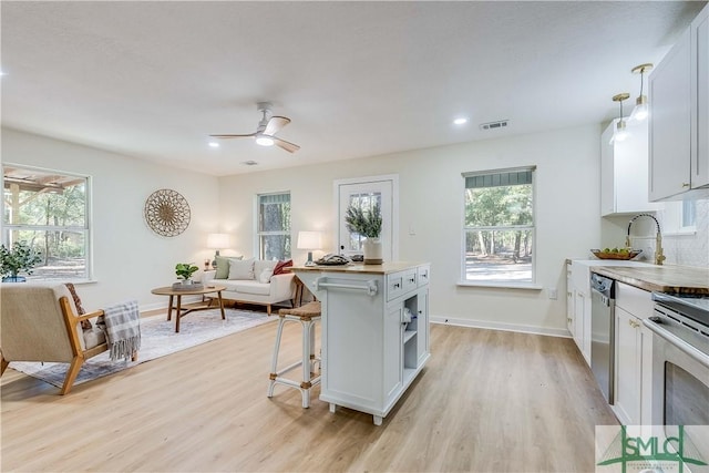 kitchen with a breakfast bar, white cabinetry, stainless steel appliances, decorative light fixtures, and light wood-type flooring