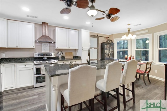 kitchen featuring double oven range, a breakfast bar area, wall chimney range hood, and white cabinets