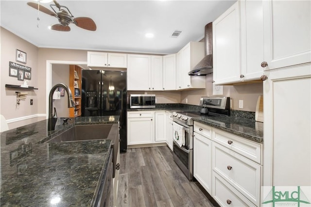 kitchen with wall chimney range hood, sink, appliances with stainless steel finishes, white cabinetry, and dark stone counters