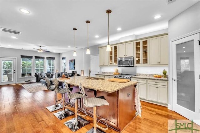 kitchen with decorative light fixtures, a center island with sink, appliances with stainless steel finishes, light stone countertops, and cream cabinetry