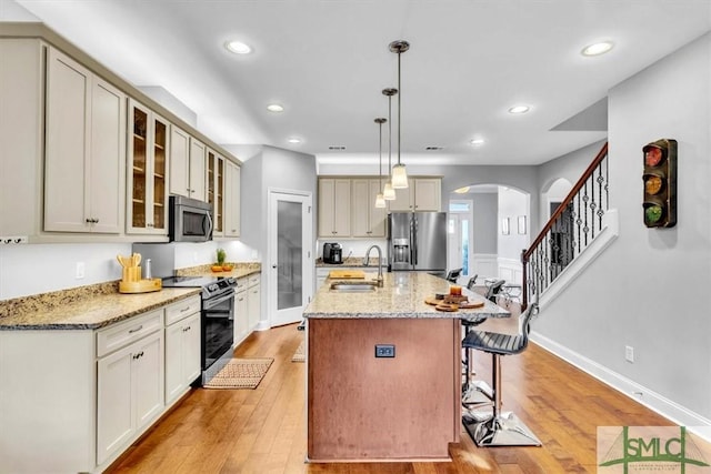 kitchen featuring sink, stainless steel appliances, light stone countertops, an island with sink, and decorative light fixtures