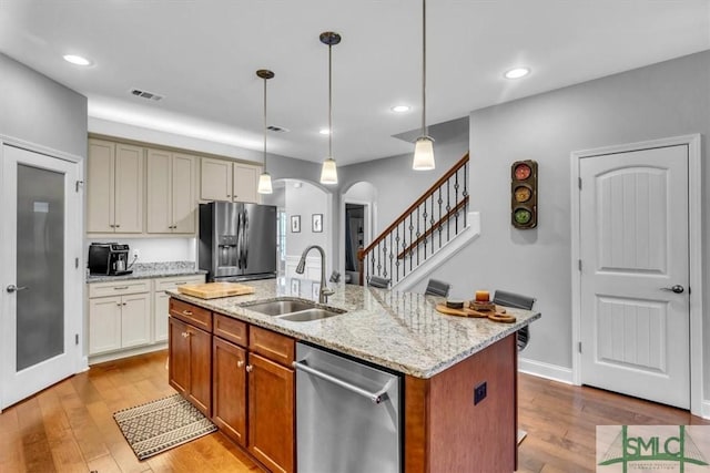 kitchen with appliances with stainless steel finishes, pendant lighting, an island with sink, sink, and cream cabinetry