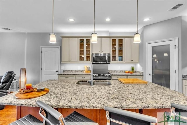 kitchen with appliances with stainless steel finishes, a kitchen bar, hanging light fixtures, a kitchen island with sink, and light stone countertops