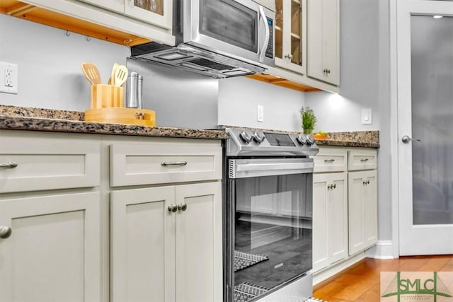 kitchen with white cabinetry, light hardwood / wood-style flooring, dark stone counters, and appliances with stainless steel finishes