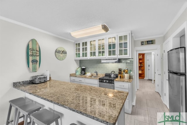 kitchen with appliances with stainless steel finishes, sink, white cabinets, a kitchen breakfast bar, and kitchen peninsula