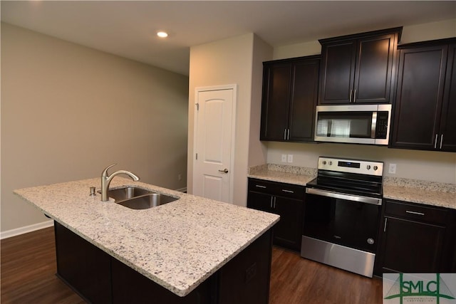 kitchen featuring dark wood-type flooring, sink, a center island with sink, appliances with stainless steel finishes, and light stone countertops