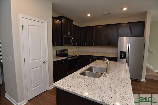 kitchen featuring appliances with stainless steel finishes, dark hardwood / wood-style floors, an island with sink, sink, and light stone countertops