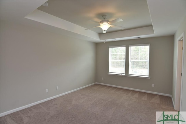 spare room featuring ceiling fan, light colored carpet, and a tray ceiling