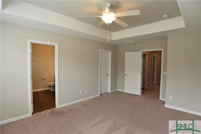 unfurnished bedroom featuring ensuite bath, ceiling fan, a raised ceiling, light carpet, and a closet