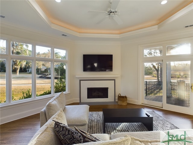 living room featuring a tray ceiling, dark wood-type flooring, ornamental molding, and ceiling fan