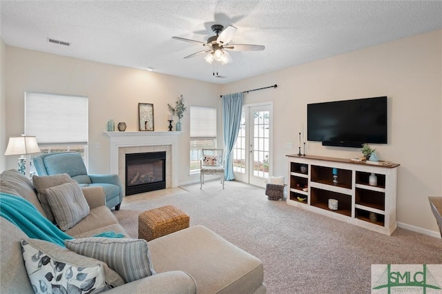 carpeted living room featuring french doors, ceiling fan, a fireplace, and a textured ceiling