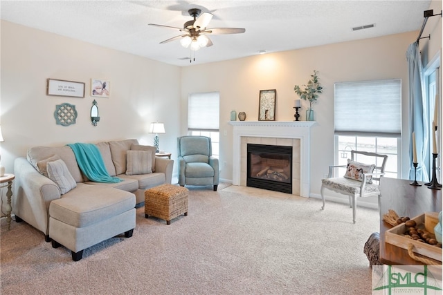 living room with a tiled fireplace, light carpet, and ceiling fan