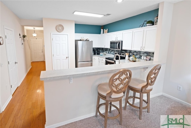 kitchen with a breakfast bar, white cabinetry, kitchen peninsula, stainless steel appliances, and backsplash