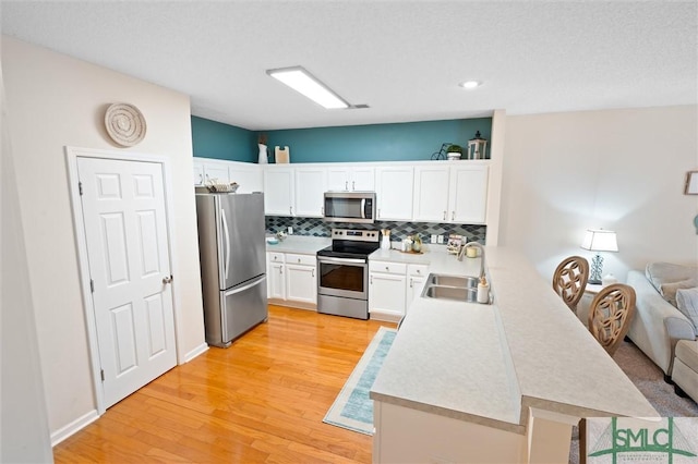 kitchen with stainless steel appliances, sink, white cabinets, and light wood-type flooring