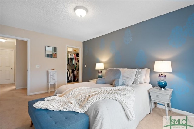 bedroom with a walk in closet, a closet, light carpet, and a textured ceiling