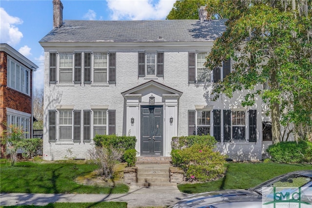 colonial inspired home with a front lawn, brick siding, and a chimney