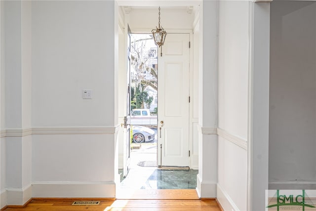 foyer featuring a notable chandelier, visible vents, baseboards, and wood finished floors