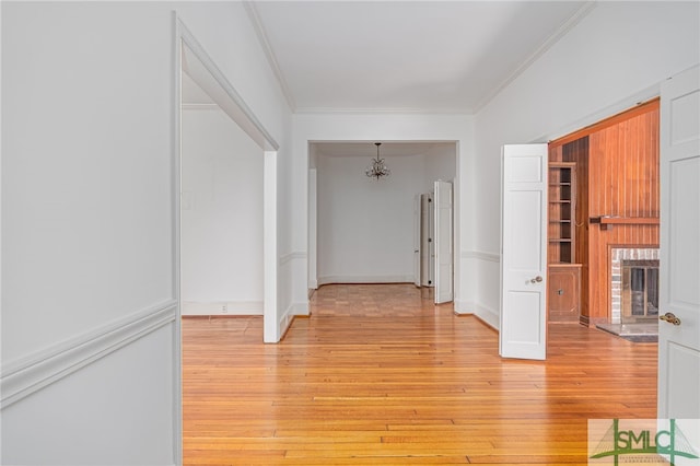 corridor with a notable chandelier, light wood-style flooring, and crown molding