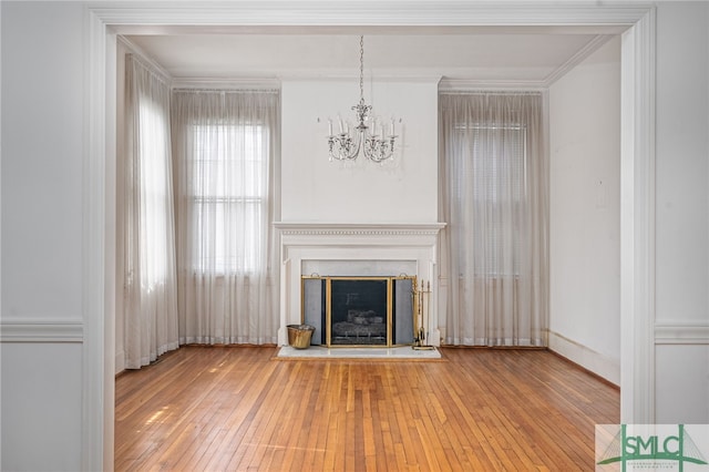 unfurnished living room featuring a fireplace with raised hearth, crown molding, an inviting chandelier, and hardwood / wood-style flooring