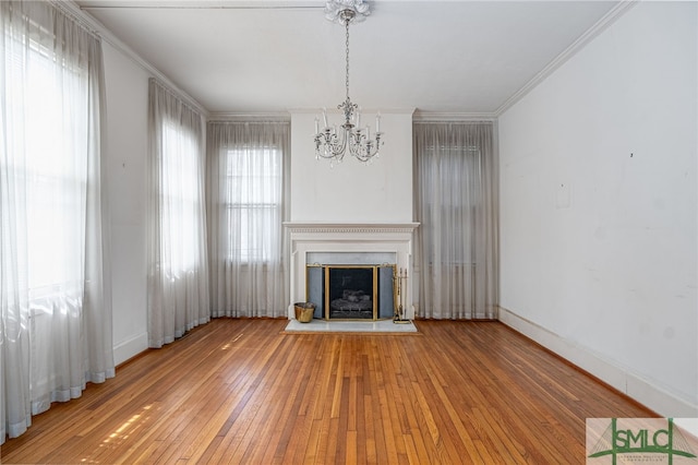 unfurnished living room with a wealth of natural light, wood-type flooring, a fireplace with raised hearth, and crown molding