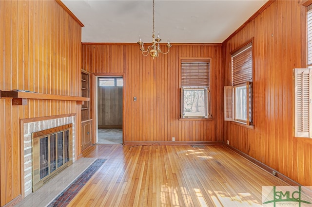 unfurnished living room featuring wooden walls, crown molding, a fireplace, a notable chandelier, and wood-type flooring