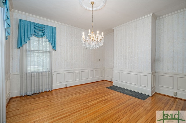 unfurnished room with wallpapered walls, crown molding, hardwood / wood-style floors, an inviting chandelier, and a decorative wall