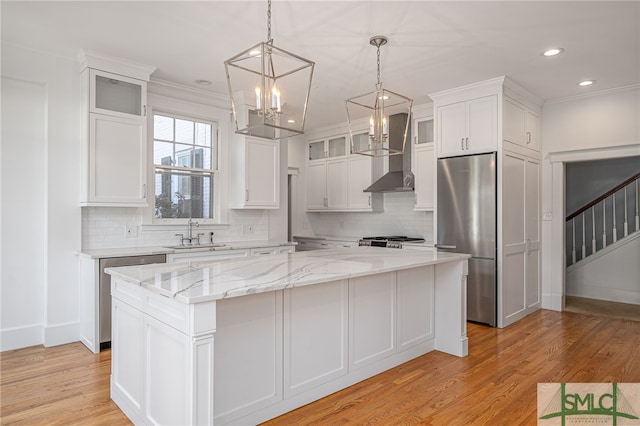 kitchen featuring a kitchen island, wall chimney range hood, stainless steel refrigerator, white cabinets, and a sink