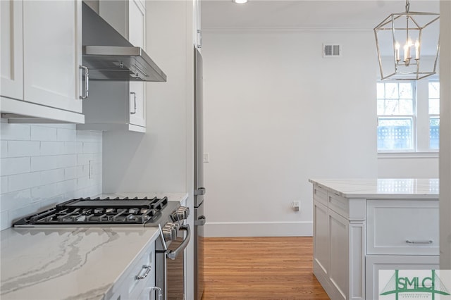 kitchen featuring white cabinetry, wall chimney exhaust hood, stainless steel gas range, and ornamental molding