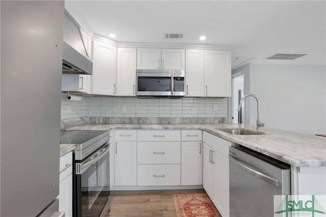 kitchen featuring sink, light stone counters, white cabinets, stainless steel appliances, and wall chimney range hood