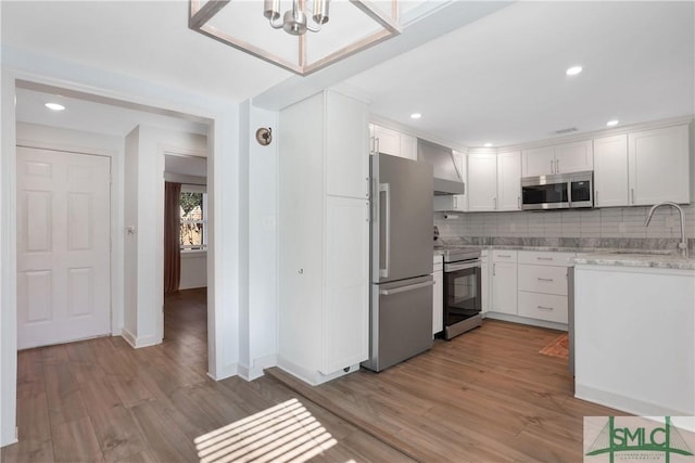 kitchen featuring white cabinetry, sink, stainless steel appliances, wall chimney range hood, and light wood-type flooring