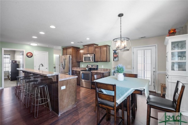 kitchen featuring sink, appliances with stainless steel finishes, a kitchen island with sink, dark hardwood / wood-style floors, and decorative light fixtures