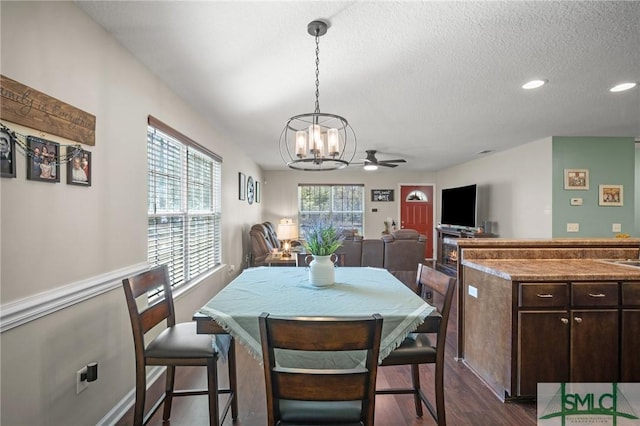 dining room with ceiling fan with notable chandelier, dark wood-type flooring, and a textured ceiling