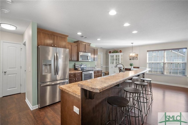 kitchen featuring appliances with stainless steel finishes, dark hardwood / wood-style floors, pendant lighting, a kitchen breakfast bar, and a kitchen island with sink