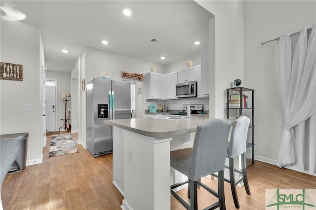 kitchen featuring light wood-type flooring, a kitchen breakfast bar, kitchen peninsula, stainless steel appliances, and white cabinets