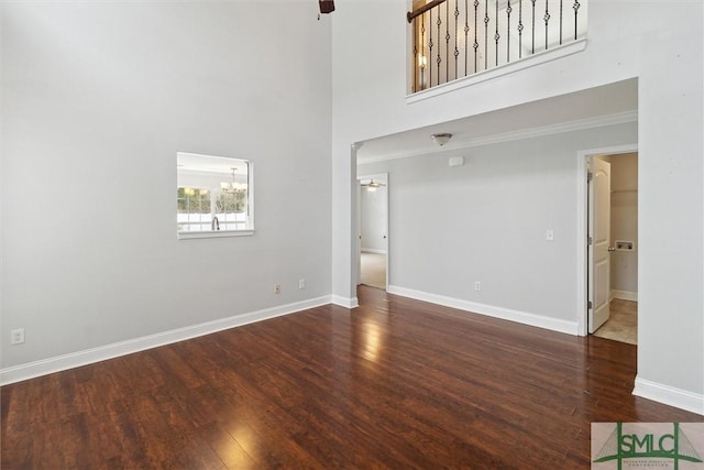 unfurnished living room with a towering ceiling, dark wood-type flooring, ornamental molding, and ceiling fan