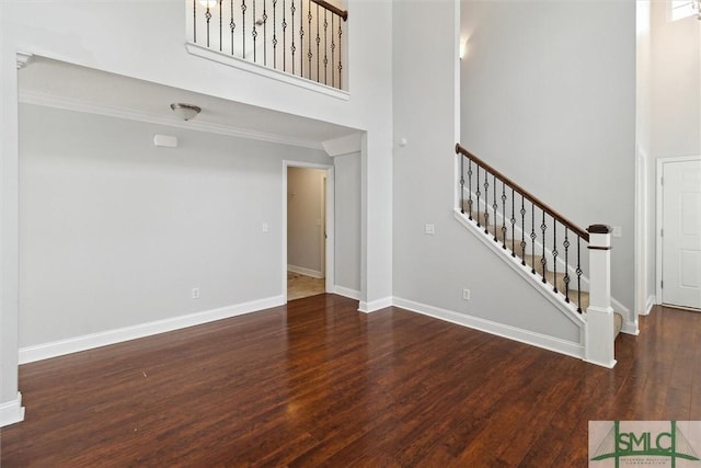 unfurnished living room featuring ornamental molding, dark hardwood / wood-style flooring, and a high ceiling