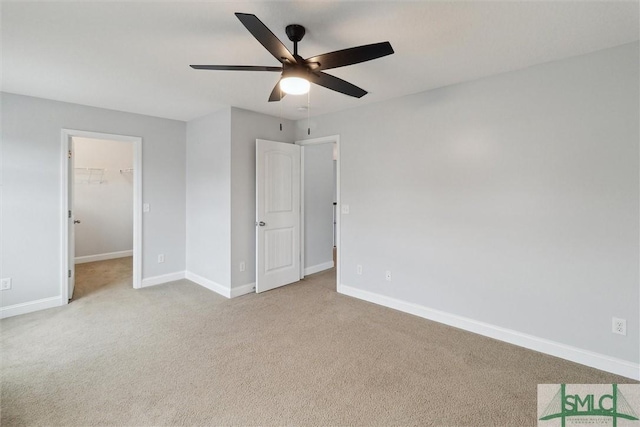 unfurnished bedroom with light carpet, a spacious closet, a closet, and ceiling fan