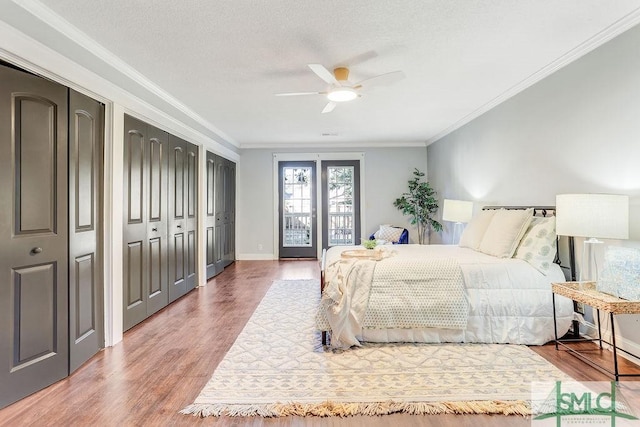 bedroom featuring crown molding, two closets, ceiling fan, access to exterior, and hardwood / wood-style floors