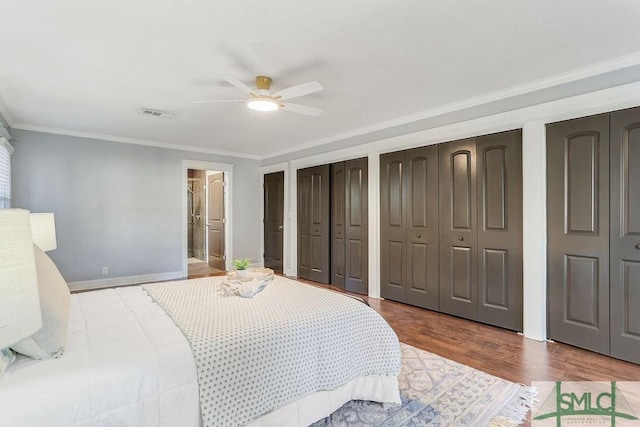 bedroom with crown molding, hardwood / wood-style flooring, ceiling fan, ensuite bathroom, and two closets