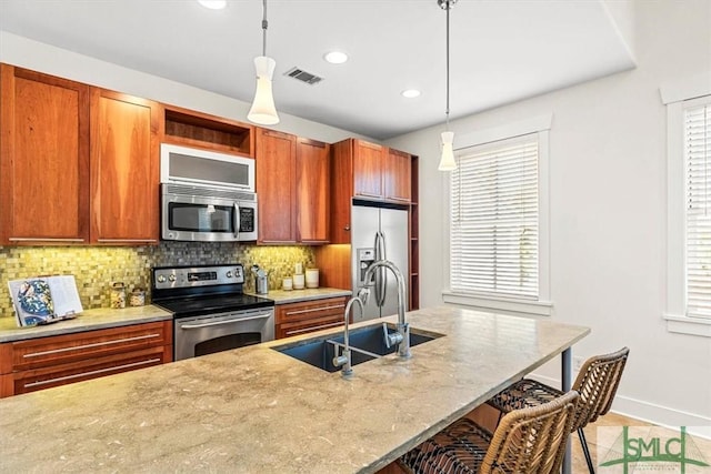 kitchen with decorative light fixtures, sink, a breakfast bar area, light stone counters, and stainless steel appliances