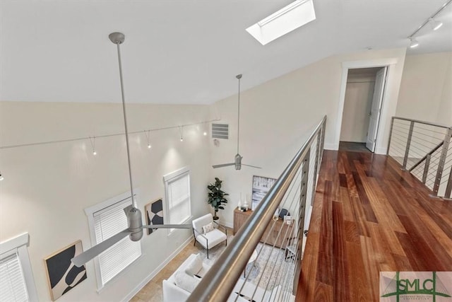 corridor with hardwood / wood-style floors, track lighting, high vaulted ceiling, and a skylight